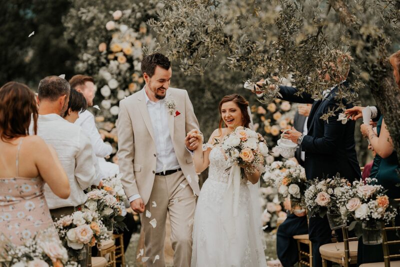 Glückliches Hochzeitspaar beim Auszug nach der Trauung in der Toskana, Blütenblätter werden geworfen.